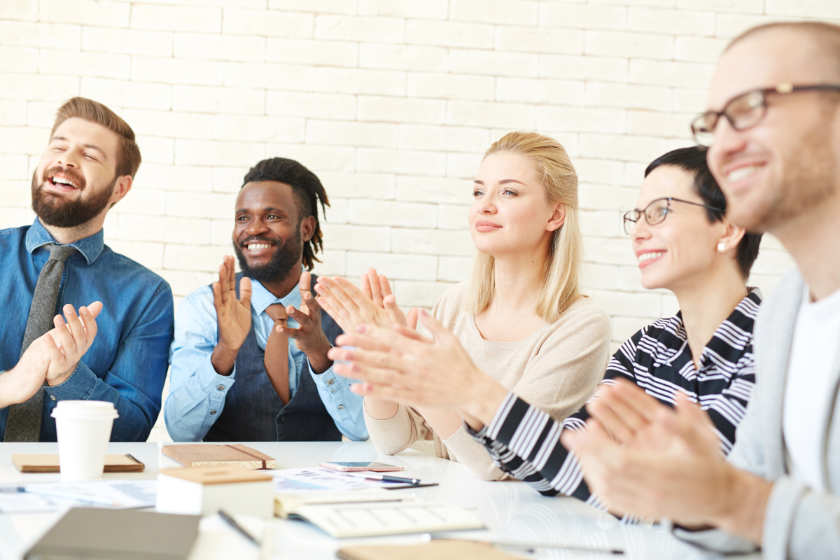 Business Team Seated Around Meeting Table Smiling and Applauding