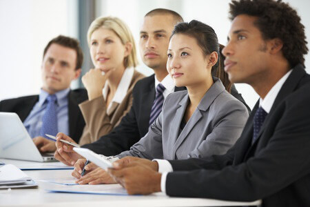 A row of diverse workers in business attire sitting on the side of a table, all of them looking in the same direction