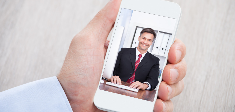 A man holding a smartphone in one hand, the screen showing someone he is video conferencing with