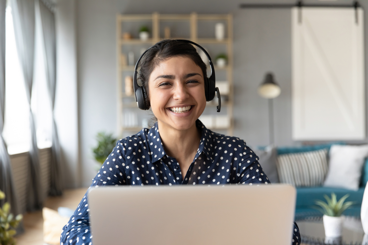 Smiling Woman Wearing Headset Seated in Front of Laptop at Home